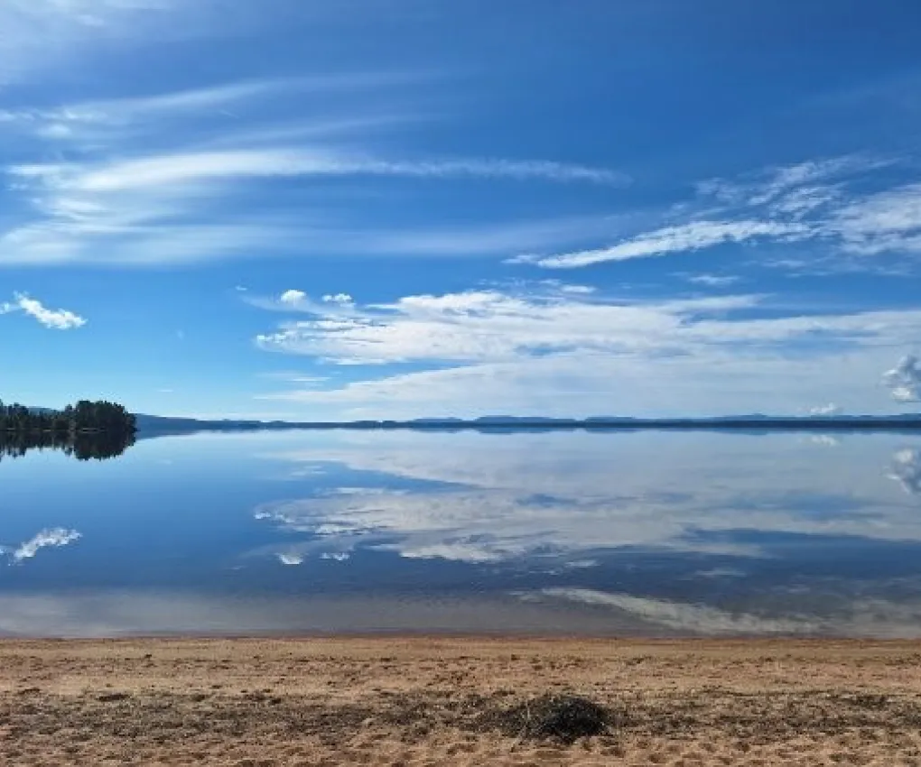 Sandstrand vid en spegelblank sjö med berg i horisonten