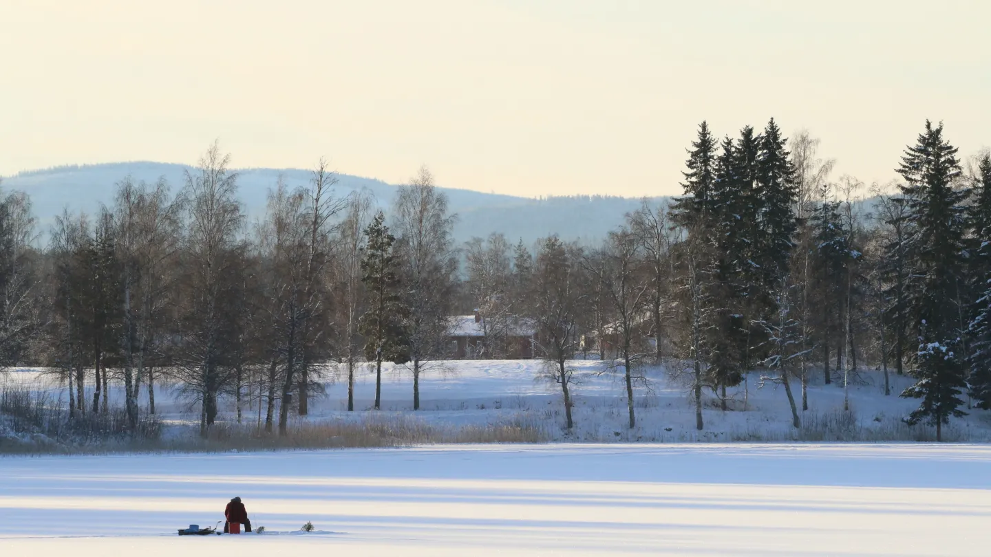 En person som sitter och isfiskar en solig dag