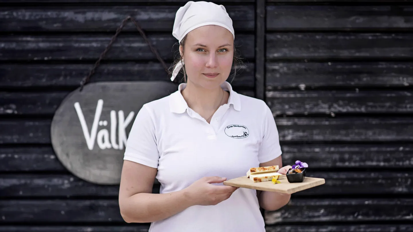 En kvinna som håller i en träbricka med ostkaka på